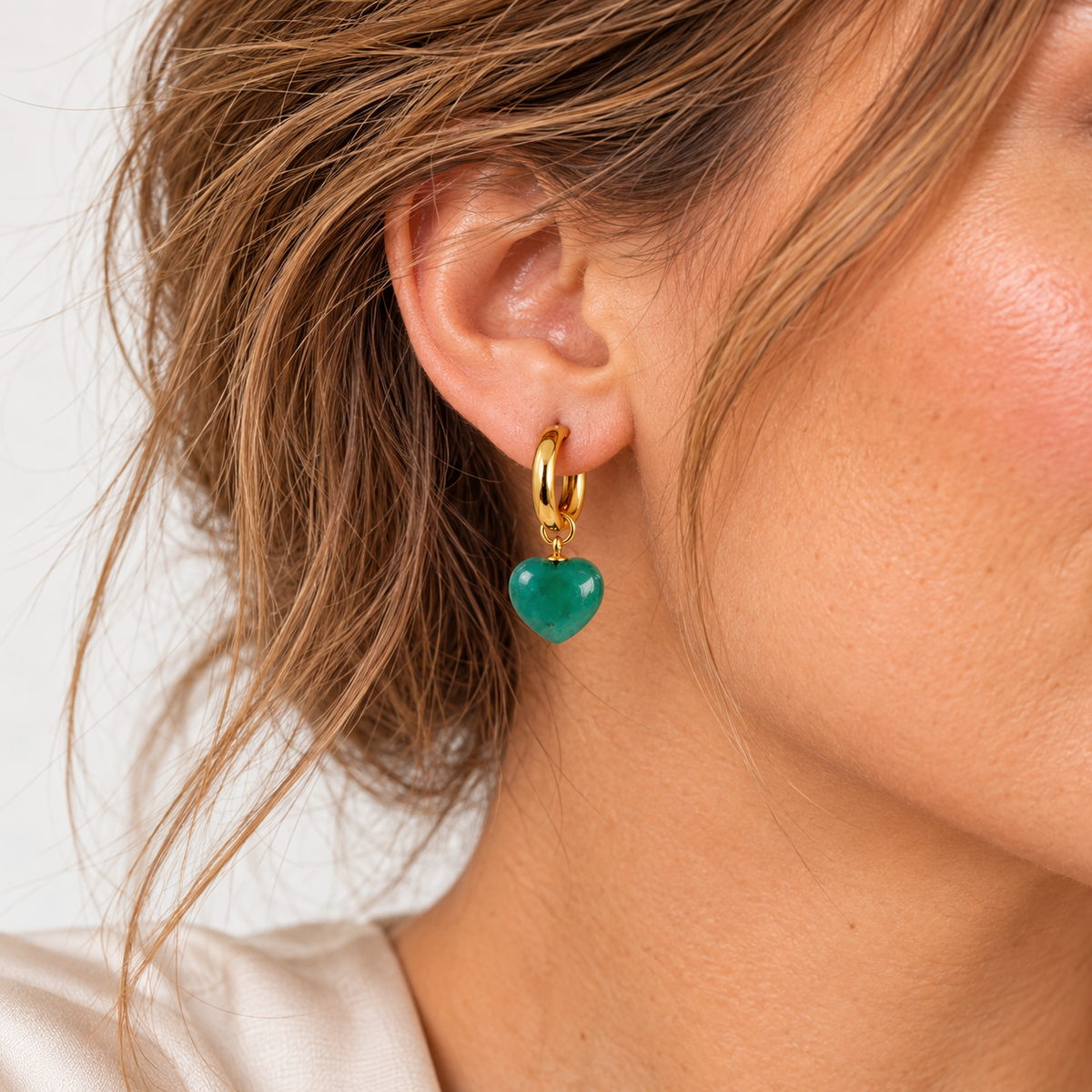Nahaufnahme einer goldfarbenen Harmony Creole mit blaugrünem Jade-Herz am Ohr.