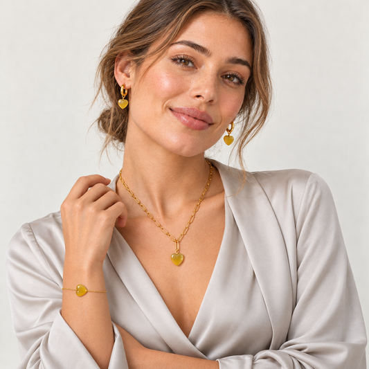 Model in hellgrauer Bluse mit goldfarbener Halskette, Creolen und Armband mit Herzen aus gelbem Achat.