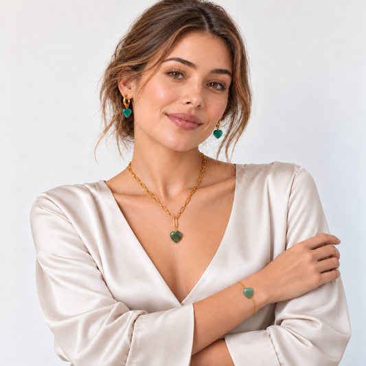Model in heller Satinbluse mit Jade-Herzschmuck: grüne Halskette, blaugrüne Creolen und hellgrünes Armband mit durchfädeltem Herz.