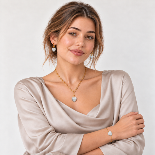 Model in heller taupefarbener Satinbluse mit goldfarbener Halskette, Creolen und Armband mit Mondstein-Herzen.