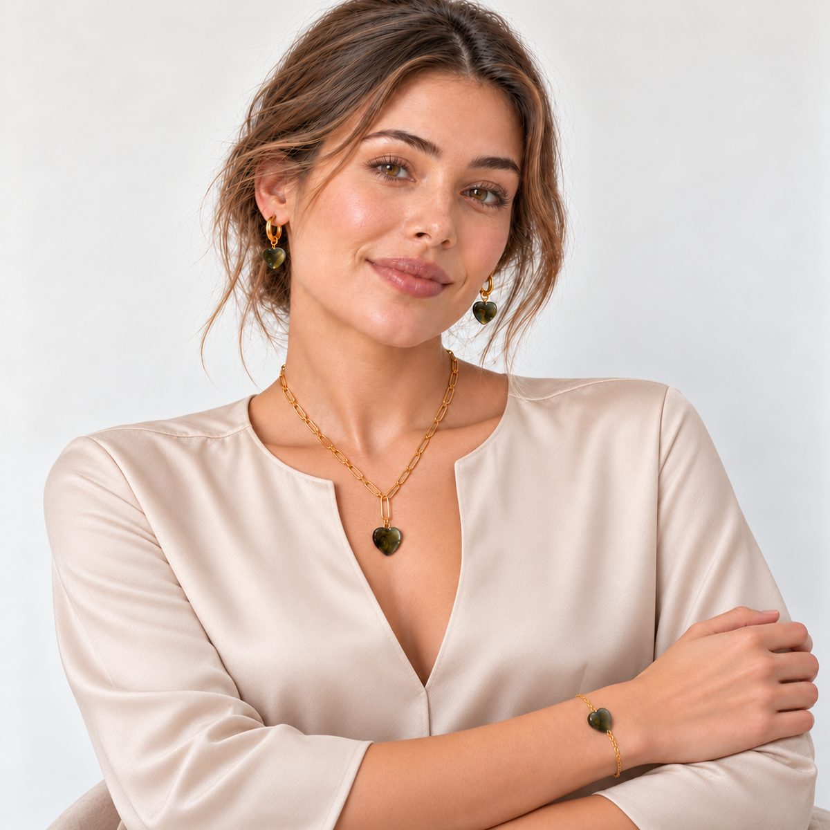 Model in schlichter champagnerfarbener Bluse mit offenem Rundhalsausschnitt und goldfarbenem Labradorit-Herzschmuck.