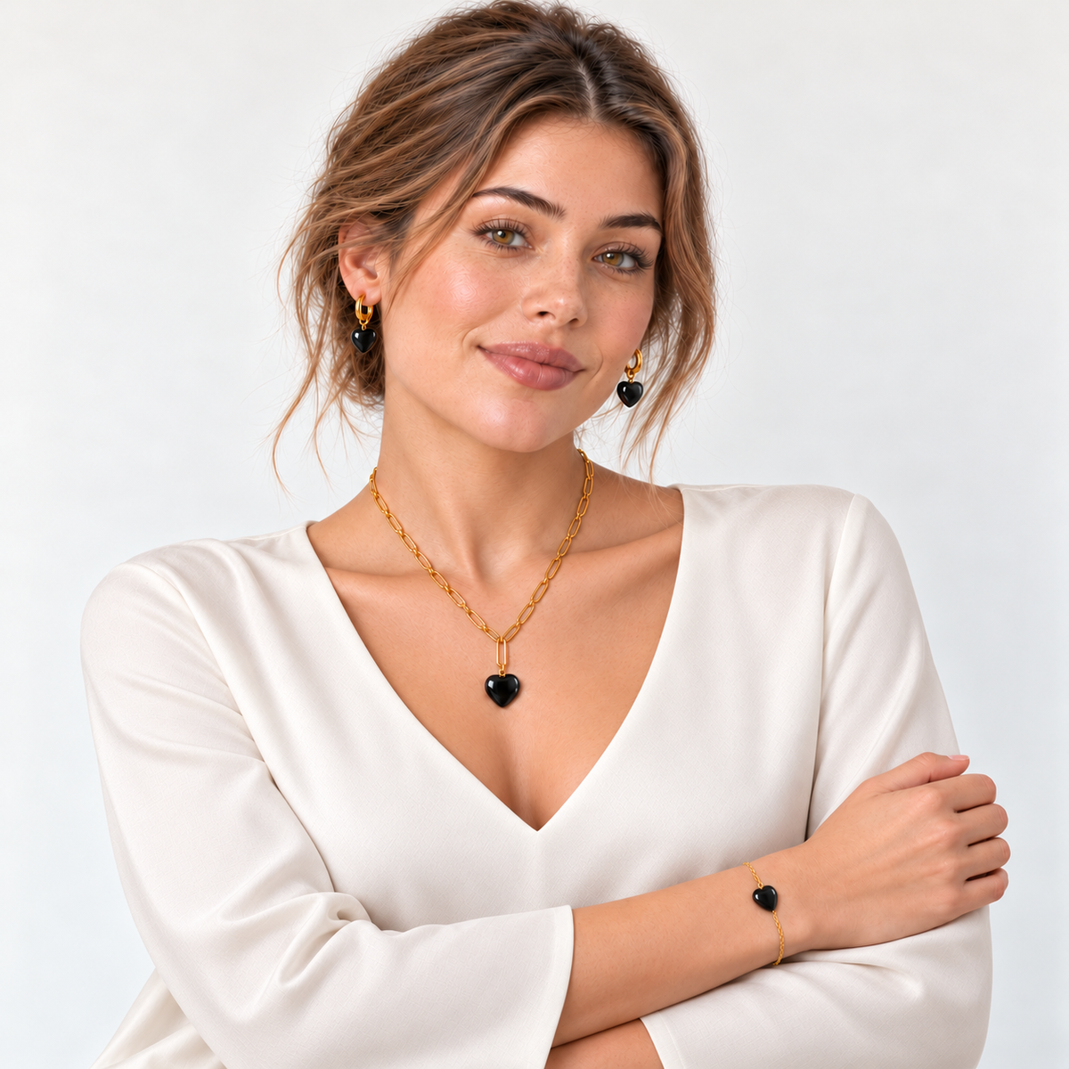 Model in schlichter elfenbeinfarbener Bluse mit V-Ausschnitt und goldfarbenem Herzschmuck aus schwarzem Achat.